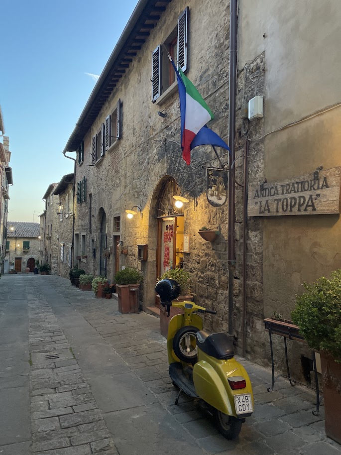 San Donato a narrow street in the medieval center with Italian flag and a vespa. Discover Secret Tuscany